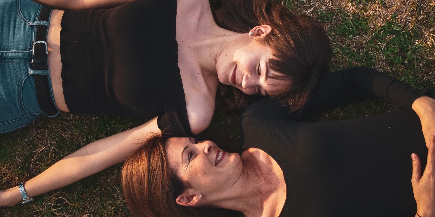 Mother and daughter lying in grass and smiling at eachother