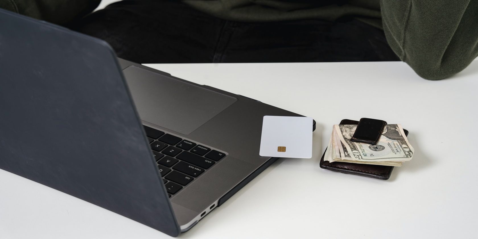 A MacBook, credit card and banknotes on a table.